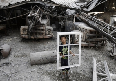Сектор Гази, Газа, 5 серпня 2014 року. Хлопчик тримає віконну раму, стоячи біля зруйнованого ракетним ударом будинку. 5 серпня Ізраїль і палестинський рух ХАМАС домовилися про 72-годинне припинення вогню після місяця обстрілів. Ізраїль вивів війська із Сектора Гази. Фото: АFР