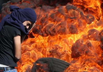 Палестинский демонстрант защищает лицо, когда он стоит перед горящими шинами во время демонстрации против экспроприации палестинских земель Израилем в селе Кафр, у Шхема в оккупированном Западном берегу, 26 октября 2014. Фото: АFР
